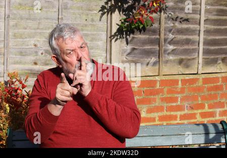 Senior or elderly man with finger to his mouth saying be quiet. Dont say it or stop the noise. Stock Photo