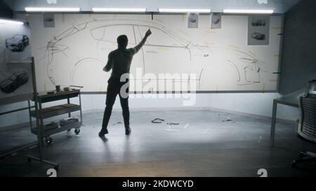 Back view of automotive african american male designer drawing sketch blueprint with marker, developing futuristic electric car design on whiteboard. Work in modern car design development studio. Stock Photo