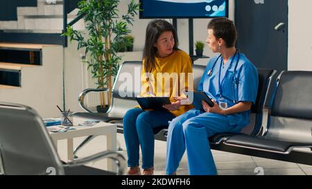 Diverse nurse and patient looking at medical report papers before attending checkup appointment with specialist. Using digital tablet and report to explain healthcare insurance support. Stock Photo