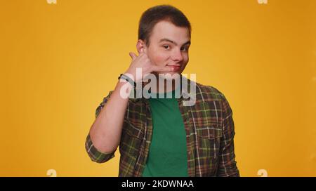 Call me please, here is contact number. Cheerful one man in shirt looking at camera doing phone gesture like says hey you call me back. Young guy boy posing isolated alone on yellow studio background Stock Photo