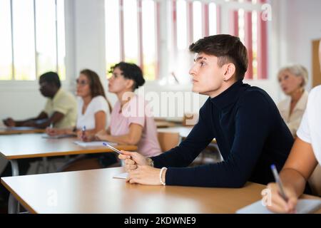 Focused guy listening and taking notes of lecture in university classroom Stock Photo