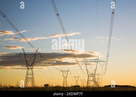 Silhouetted electricity transmission towers in field at sunset in summer, Monteregie, Quebec, Canada. Stock Photo