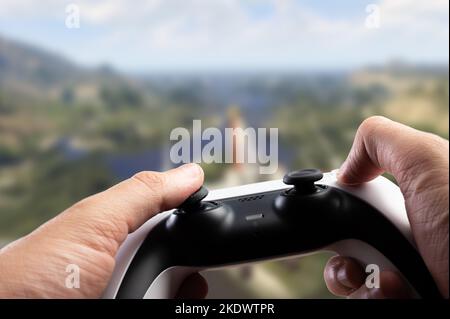 A modern GAM22ICB gamepad in the hands of a gamer against the backdrop of a large screen with an adventure video game. Hobbies, recreation, communicat Stock Photo