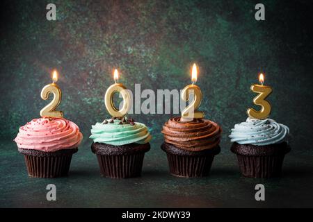 Cupcakes with golden lit number candles for the New Year 2023. Stock Photo