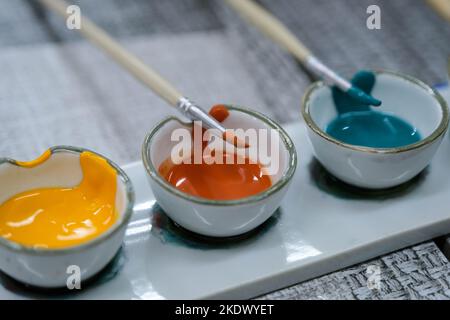 Watercolor in a small ceramic cup with a brush on the table for art work. Stock Photo