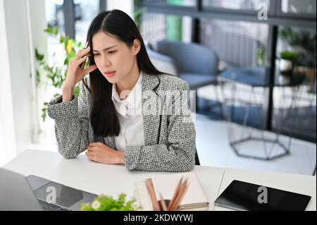 Stressed young Asian businesswoman or female manager checking her work on laptop screen, pensive thinking and planning new strategy. Stock Photo