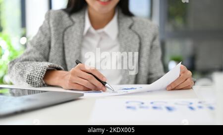 Beautiful millennial Asian businesswoman or female financial analyst checking financial data on the report, analyzing business financial data, working Stock Photo