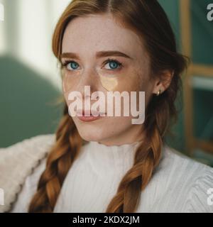 Portrait of a beautiful redheaded woman with blue eyes and under-eye patches sitting indoors. Concept of rest. Home bedroom Stock Photo