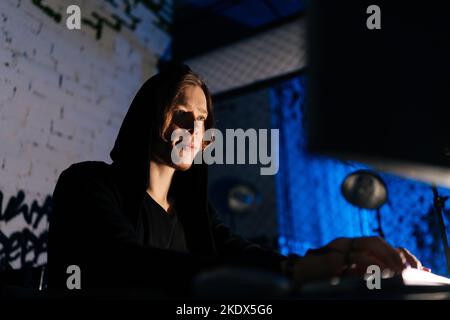 Close-up view of dangerous hacker man in sweatshirt hacking online web site or engaging hacking into security systems, using laptop and desktop Stock Photo