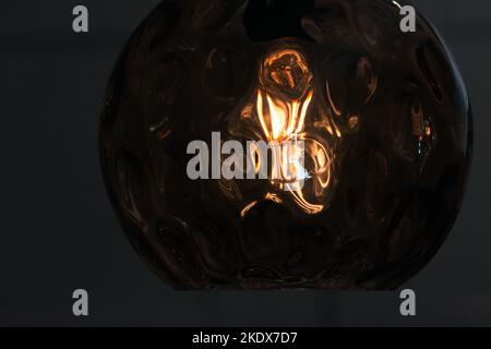 Round glass lampshade with a tungsten lamp glows in the dark, close-up photo with selective soft focus Stock Photo