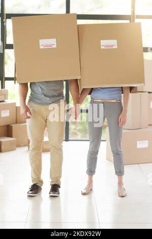 Having fun while unpacking. a carefree young couple posing with boxes on their heads while moving into their new home. Stock Photo