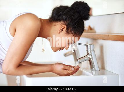 Stick to a routine that works for your skin. a young woman washing her face in the bathroom. Stock Photo