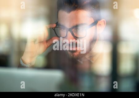 Hes got this project in his sights. a focused young programmer working on his computer behind a glass wall. Stock Photo
