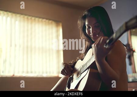 No audience required. a happy young woman playing her guitar while sitting on her bed. Stock Photo