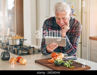 Watching a step-by-step tutorial of the recipe hes trying out. a senior man using a digital tablet while cooking in his kitchen. Stock Photo