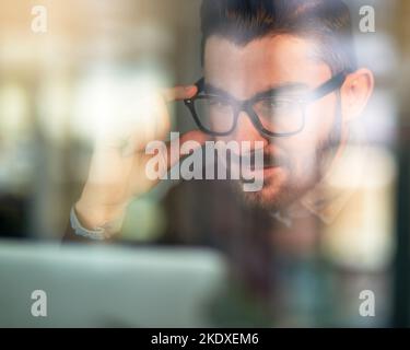 He works hard to accomplish his goals. a focused young programmer working on his computer behind a glass wall. Stock Photo
