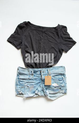 A gray t-shirt and denim shorts lie on a white background with a tag for a price, clothing sale, business and clothing store Stock Photo