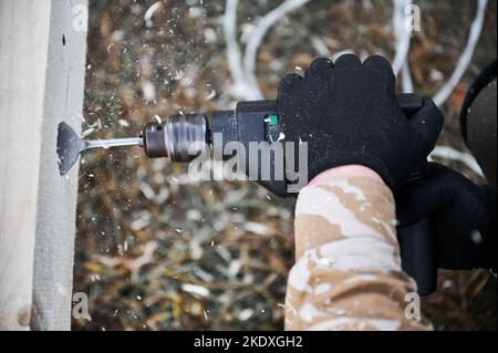 Man building wooden frame house. Close up of male worker drilling hole by electric drill in timber framing of future house on construction site. Carpentry concept. Stock Photo