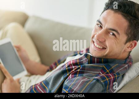 The smart way of staying stress-free. Portrait of a relaxed young man using a digital tablet on the sofa at home. Stock Photo