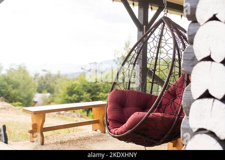 Rattan wicker cocoon garden swing chair hanged on frame. Recreation scene with a hammock-chair in the backyard of the house. A cozy place to relax Stock Photo