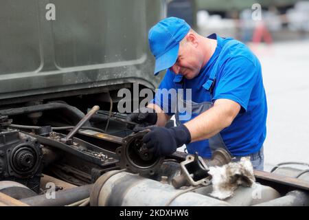 Mechanic in overalls repairs truck on summer day outside. Urgent repair of trucks. Authentic workflow.. Stock Photo
