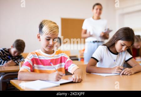 Focused preteen schoolboy writing in workbook during lesson Stock Photo