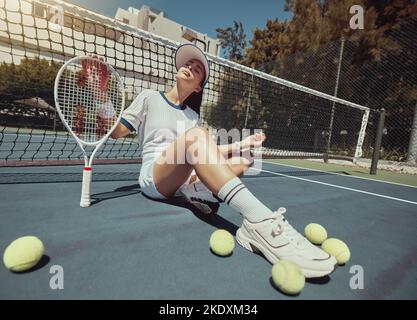 Tennis, sports and exercise with a woman athlete sitting on a court with a racket and balls after a game. Fitness, sport and training with an Stock Photo