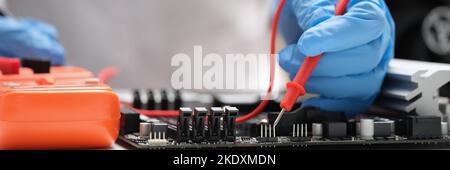 Technician measuring voltage of in computer mainboard using electronic digital multimeter Stock Photo