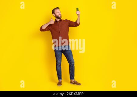 Full body of positive attractive guy hold telephone take selfie show thumb up isolated on yellow color background Stock Photo