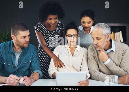 Connecting their strategy to their execution. a group of colleagues discussing something on a digital tablet together. Stock Photo