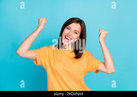 Photo of optimistic satisfied pretty girl with straight hairdo dressed yellow t-shirt raise fists isolated on blue color background Stock Photo