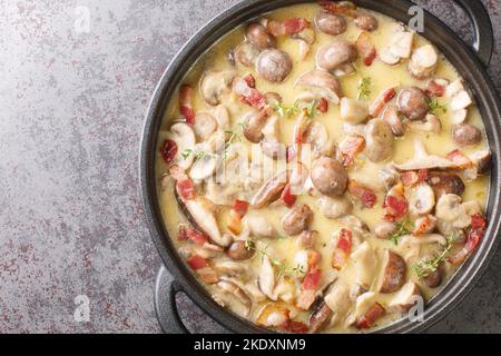 Stewed Champignon mushrooms in a spicy creamy wine sauce with bacon and parmesan cheese close-up in a frying pan on the table. Horizontal top view fro Stock Photo