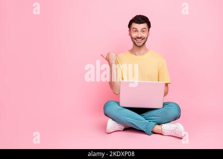 Photo of positive man wear stylish clothes sit arm direct empty space recommend fast connection wifi isolated on pink color background Stock Photo