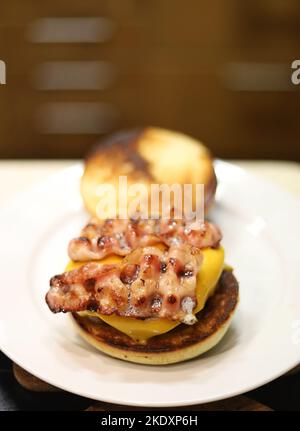 High angle of appetizing juicy hamburger with grilled bacon and cheese served on white plate placed on table Stock Photo