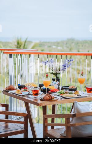 Table setting with delicious fruits and fresh buns with drinks on terrace of tropical resort hotel in morning Stock Photo