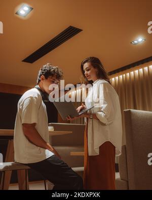 Modern smart casual female using laptop standing next to guy in glasses while standing in cafe and working remotely Stock Photo