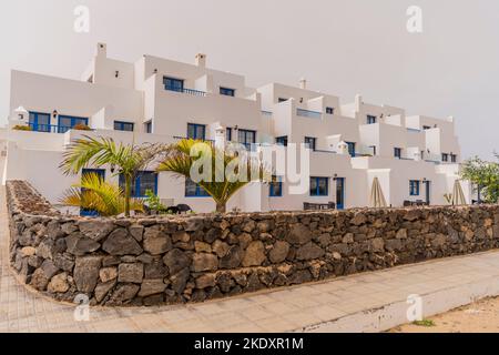 White houses and green palm trees located behind stone fence against gray sky on street in Lanzarote, Canary Islands, Spain Stock Photo