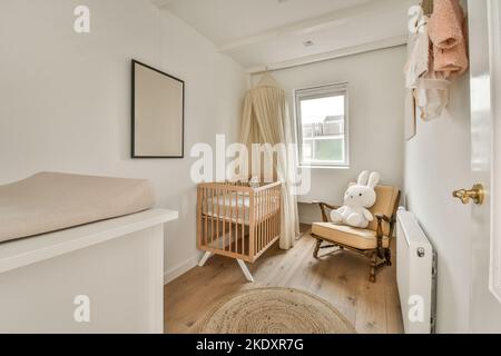 Crib placed at wall near window in light spacious children bedroom with chest of drawers with lamp at home Stock Photo