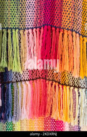 Background of multicolored carpet weaved on loom with knotted threads hanging on ropes in workshop Stock Photo