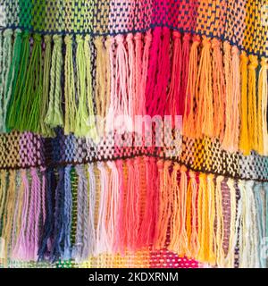 Background of multicolored carpet weaved on loom with knotted threads hanging on ropes in workshop Stock Photo