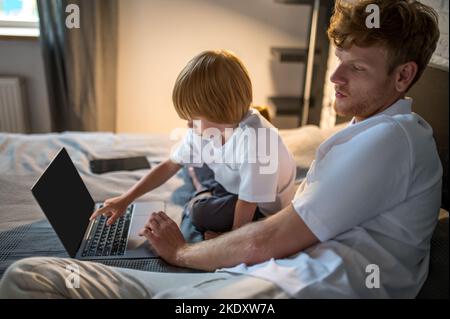 Dad and son lying in bed and watching something online before sleep Stock Photo