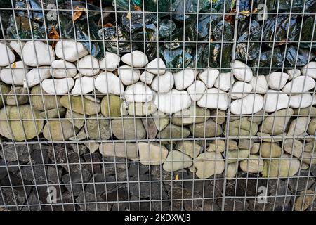 Strong wall with different stones made from pebbles inside of galvanized wire. Stock Photo