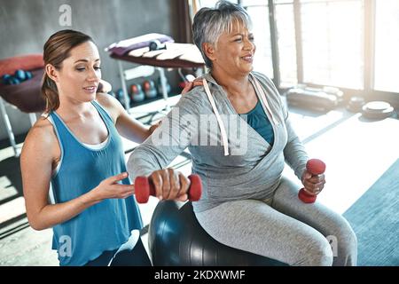 Building balance and strength for a better quality of life. a senior woman using weights and a fitness ball with the help of a physical therapist. Stock Photo