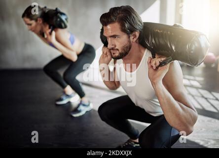 Giving up is simply not an option. two young people working out in the gym using weighted bags. Stock Photo