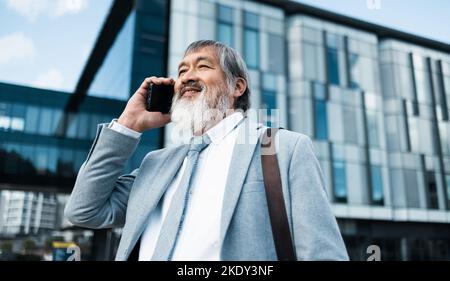 Asian leader, senior man, phone call and communication for business, connect or conversation outdoor. Leadership, smartphone and senior male talking Stock Photo