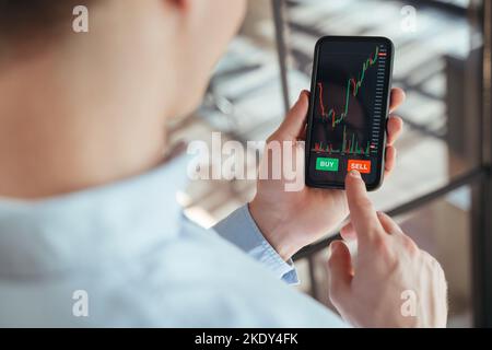 Closeup no face image of trader going to press sell button on smartphone with cryptocurrency app, after analyzing stock exchange market or crypto currency data, holding smartphone in hands Stock Photo