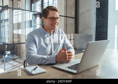 Attractive smiling entrepreneur looking at laptop screen with enthusiasm, having online conference with partners, discussing trading strategy. HR manager video call Stock Photo