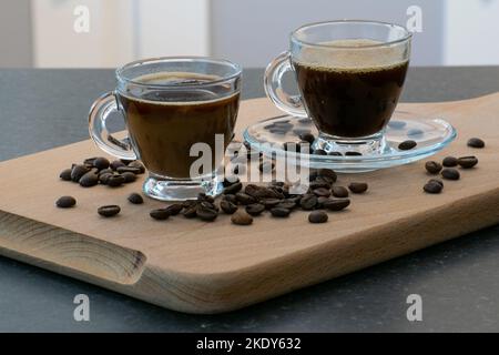 A couple of cups of coffee drinks in clear cups and beans spilled on a wooden board Stock Photo