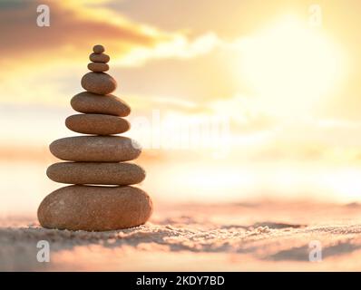 Balanced pebble pyramid on the beach. Abstract warm sunset bokeh with sand on the background. Zen stones on the sea beach, balance concept. Stock Photo
