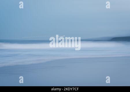 Slow shutter movement ICM of blue sunset at Tynemouth Longsands beach in North Tyneside with the lighthouse light trails across the waves Stock Photo